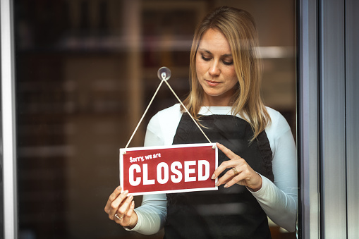 Portrait of a Caucasian woman with black apron,  holding a door sign ''sorry, we are closed''