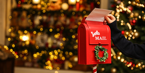 child's hand puts a letter to santa claus in the mailbox