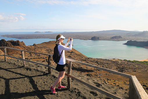 Sullivan Bay, Galapagos Islands, Ecuador - March 27, 2018: A woman taking a picture of the view atop a mountain on Bartolome Island in the Galapagos