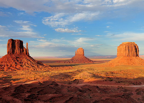 View To The East Mitten Butte, Merrick Butte And West Mitten Butte In The Monument Valley Arizona In The Late Afternoon Sun On A Sunny Summer Day With A Clear Blue Sky And A Few Clouds