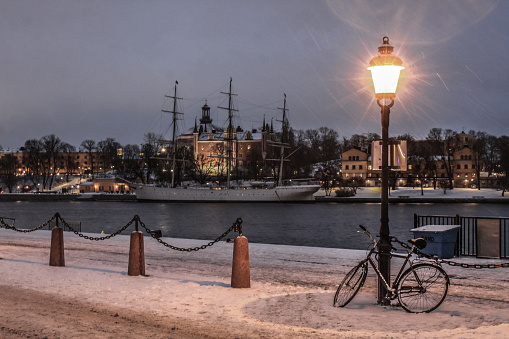 Evening shot during snowfall in the ferry port of the old town, Gamla Stan. In the background is Skeppsholmen and the Modern Museum on the other side of the Stockholm stream.\n\nGamla Stan until 1980 was officially Staden mellan broarna (\