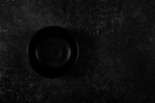 top artistic view of empty black plate on dark black background. There is copy space at right side for advertisement.  Shot with DSLR Canon 5DSR and Sigma 35mm ART series