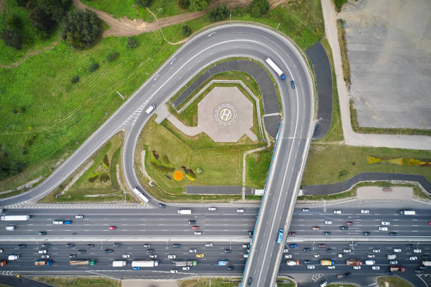 aerial top down horizontal view of the multiple lane highway and overpass. helipad inside the exit. traffic jam on the road. green tress, plantings and fields at sides all around. camera looks down directly above the highway. - multiple lane highway highway car field imagens e fotografias de stock