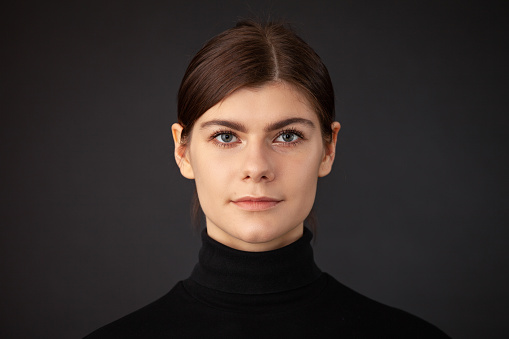 Close up studio portrait of 20 year old woman with brown ponytail hair in a black sweater on a black background