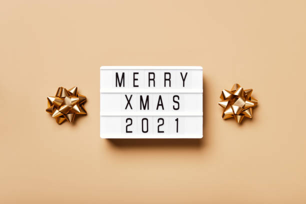 istock Lightbox with text MERRY XMAS 2021 and golden christmas decor on beige background. Creative layout in neutral monochrome colors 1287119848