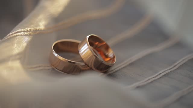 Two gold wedding rings lying on white-gray surface of dress shining with light close up macro