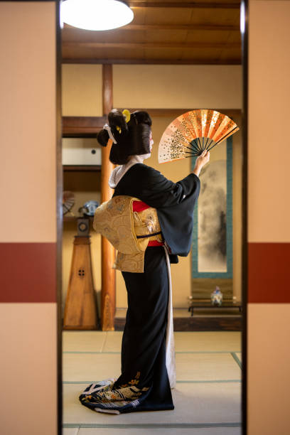 japanese 'geisha' woman in black and gold kimono dancing with folding paper fan in japanese 'tatami' room - camel back imagens e fotografias de stock