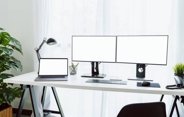 istock Nice desk in home, computer and laptop with blank screen on table in home on the day light shone in the afternoon. 1287128608