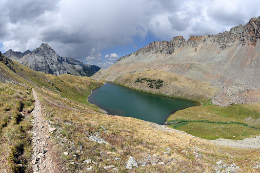Hiking trail and colorful Middle Blue Lake seen from a hiking trail towards the highest, Upper Lake near Mt Sneffels in the Rocky Mountains. This is Mount Sneffels Wilderness of Uncompahgre National Forest, near the City of Ouray, Colorado, United States.
