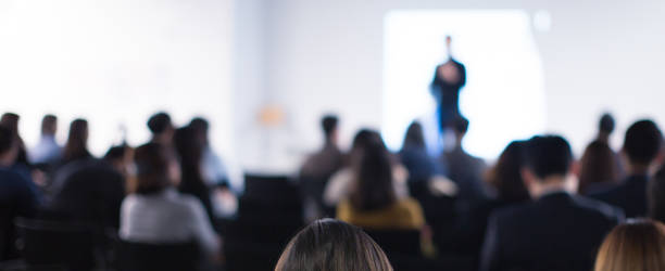 speaker on the stage with rear view of audience in the conference hall or seminar meeting, business and education concept. speaker giving a talk at business meeting. seminar presentation photo. - seminar imagens e fotografias de stock