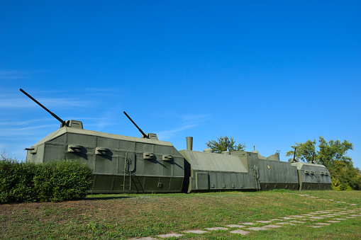 Green armored train with several guns stands on a hill against a blue sky