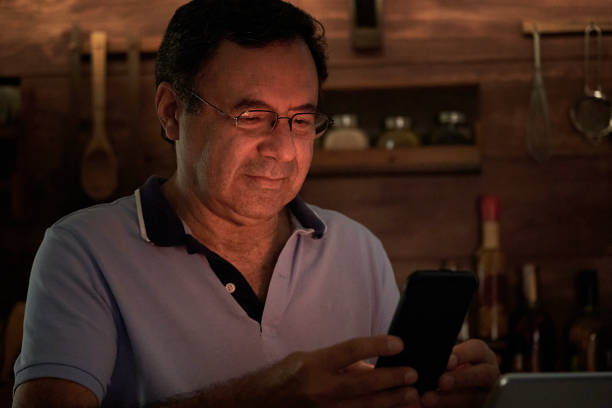 istock Senior Hispanic man using smart phone in a domestic kitchen home office with low lighting 1287145868