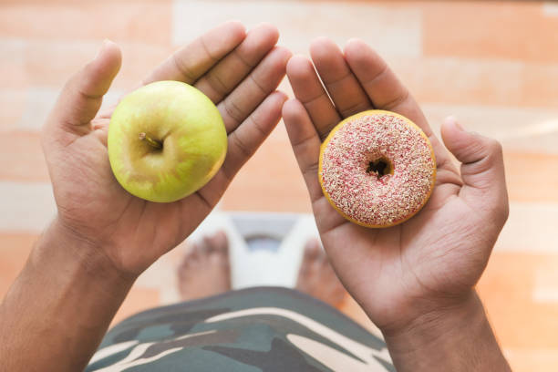 istock hand holding donuts and apple on hand on weight scale . 1287146804