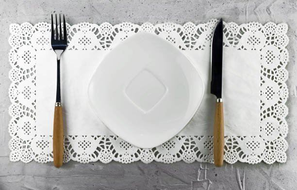 istock Empty white ceramic plate with a knife, fork, on a napkin on a gray background, close-up 1287152688