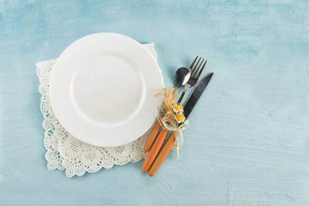 istock Empty white ceramic plate with a knife, fork, spoon on an old wooden table made of boards with a natural pattern, close-up 1287152695