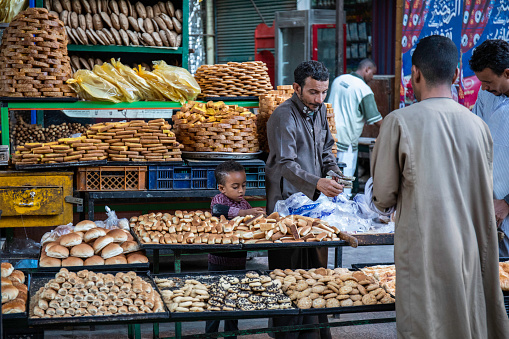 An Egyptian man in traditional clothing selling baked goods with his son's help,