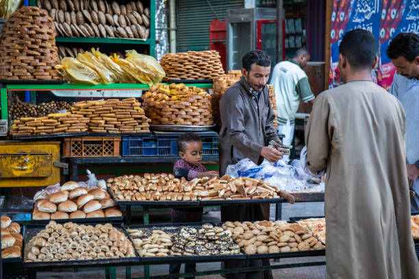 A street market bakery selling pastries, Aswan, Egypt. An Egyptian man in traditional clothing selling baked goods with his son's help, aswan egypte stock pictures, royalty-free photos & images