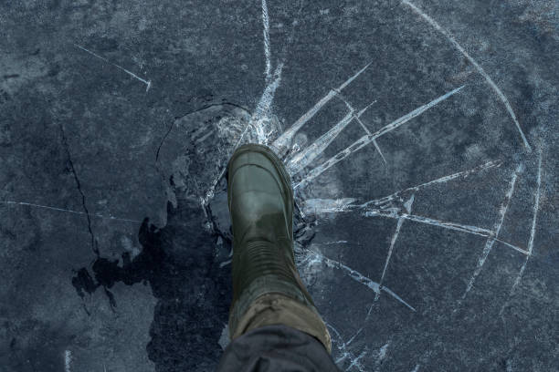 fisherman foot on broken cracked thin ice at lake. dangerous winter fishing - thin imagens e fotografias de stock