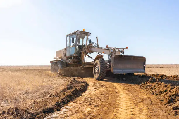 Photo of grader machine making a new road, dig the gravel dirt in the field