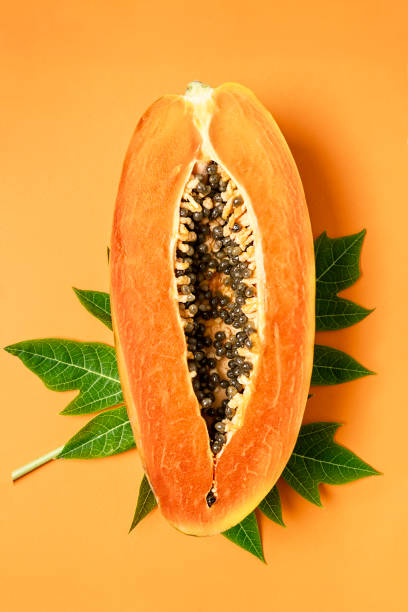istock Ripe freshly cut papaya fruit with green leaf on orange background, flat lay, copy space, vertical composition 1287161025
