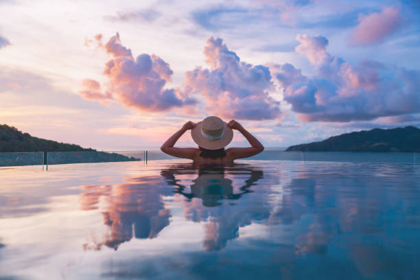 Asian travel bikini woman relax in infinity pool on phuket beach Thailand Summer travel vacation concept, Happy traveler asian woman with hat and bikini relax in luxury infinity pool hotel resort with sea beach at sunset in Phuket, Thailand luxury lifestyle stock pictures, royalty-free photos & images