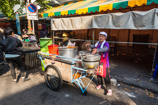 Bangkok, Thailand - December 7, 2019: Local woman with his cart selling hot food on the streets of Bangkok, Thailand.