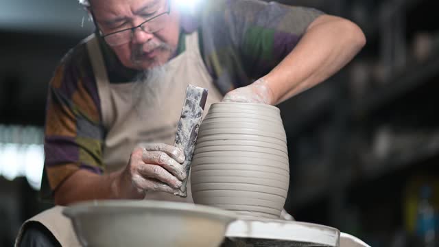 Asian chinese senior man clay artist working in his studio with spinning pottery wheel
