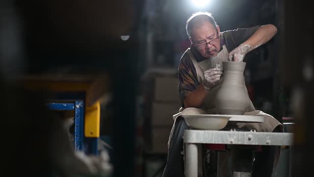 Asian chinese senior man clay artist working in his studio with spinning pottery whee