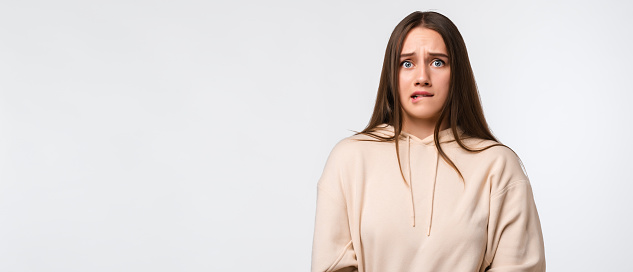 I'm afraid. Fright, phobia, panic attack, horror. Portrait of the scared woman with long chestnut hair, wearing stylish beige hoodie, isolated on white background. Copy space for your text