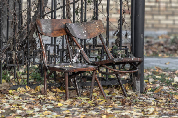 Two empty chairs. Old wooden furniture. Broken chairs. Discarded rags. Autumn wilting. Two items. Outdoor interior items. A symbol of loneliness and old age. The concept of emptiness and uselessness.