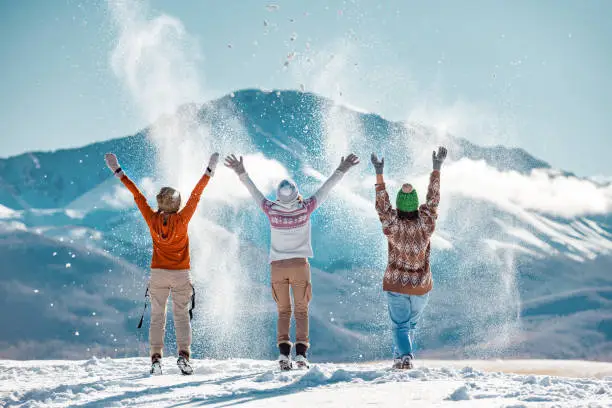 Photo of Three happy girls throw first snow on background of mountains