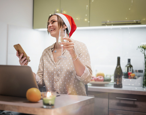 young happy woman in santa hat celebrating christmas and new year online using laptop with glass champagne