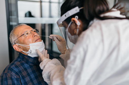 Female doctor in protective suit taking nose swab test from senior man