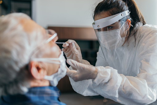 Mujer doctora en traje protector tomando prueba de hisopo de nariz de hombre de la tercera edad photo