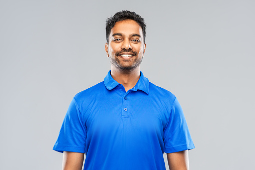 emotion, expression and people concept - smiling indian man in blue polo shirt over gray background