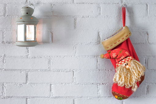 A red sock for a Christmas gift and a lamp with a candle hang on a white brick wall in the house