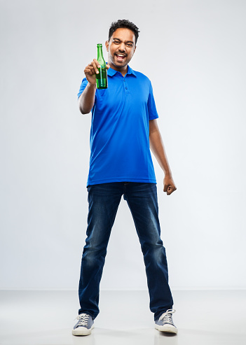 emotion, expression and success concept - happy indian man or sports fan beer bottle celebrating victory over grey background