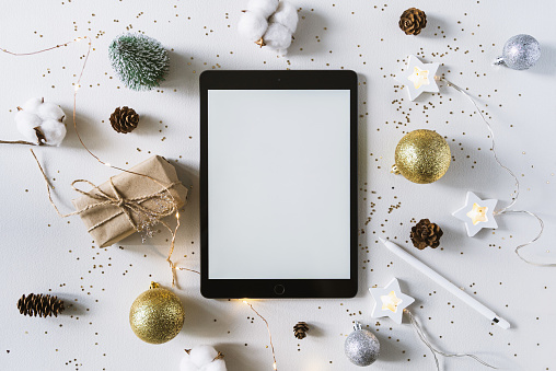 Christmas festive decorations and the tablet with pencil. With wish list and  goals concept. Tablet mock up, gift, and coton branch with shiny golden balls.New year flat lay, top view, copy space.