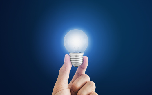 Hand holding glowing light bulb, on blue background