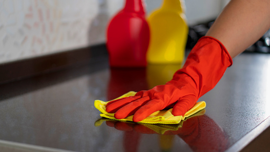 Employee hand in rubber protective glove with microfiber rag wiping black table, wall or floor surface in room, bathroom, kitchen. Early spring or regular cleanup. Commercial cleaning company concept