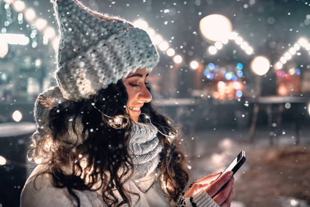 Pretty girl wearing a knitted scarf and hat holding a smartphone. Merry Christmas and Happy New Year to your loved ones and family. Festive night city lights and garlands background. Pretty girl wearing a knitted scarf and hat holding a smartphone. Merry Christmas and Happy New Year to your loved ones and family. Festive night city lights and garlands background. female magician stock pictures, royalty-free photos & images