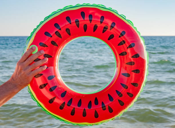 istock male hand with an inflatable swimming circle with a watermelon pattern on the background of the sea. summer holidays, travel 1287196502