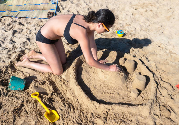 ragazza adolescente bruna in costume da bagno al mare. il ritratto della giovane di circa 13-16 anni. l'adolescente costruisce castelli di sabbia in fondo al mare. giornata di sole e mare. vacanze di viaggio d'infanzia. - teenager 14 15 years 13 14 years cheerful foto e immagini stock