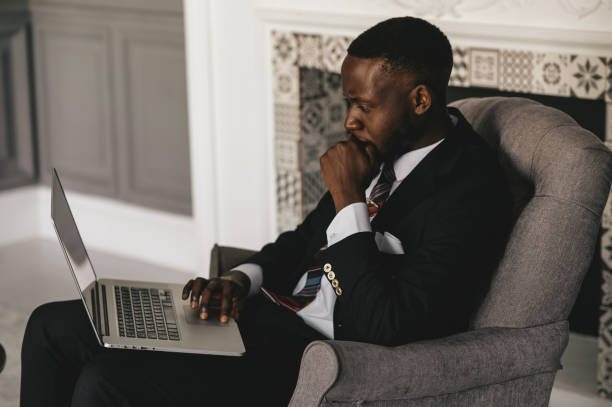 istock black guy in a black suit stares hard at a laptop 1287199212