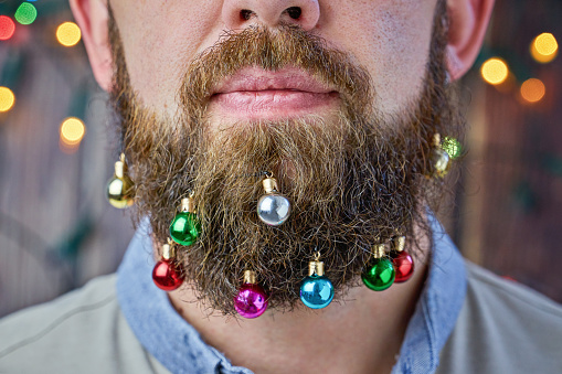 Close up of hipster man with colorful beard baubles Christmas ball in beard. Trendy x-mas decorations for facial hairs, cropped photo