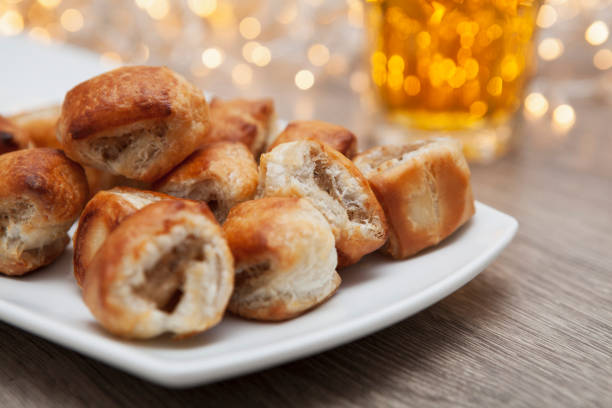 Close-up of sausage rolls on a white platter with beer and party lights A celebration at home - party food and drink with festive lights sausage roll stock pictures, royalty-free photos & images