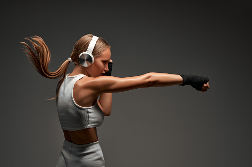 Sporty female boxer with headphones on grey background. Side view.