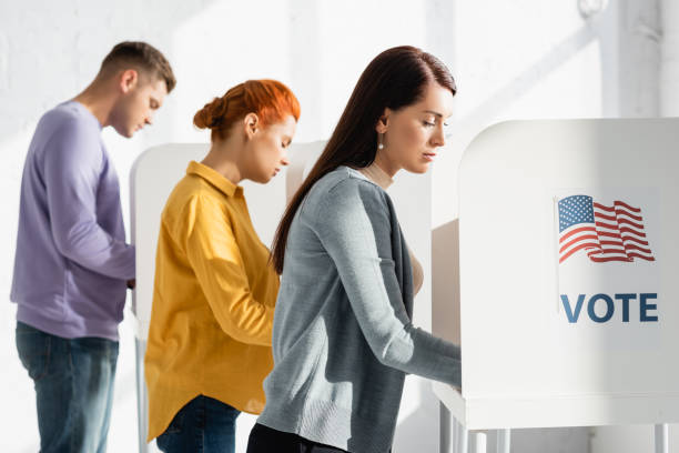voters in polling cabins with american flag and vote lettering on blurred background stock photo
