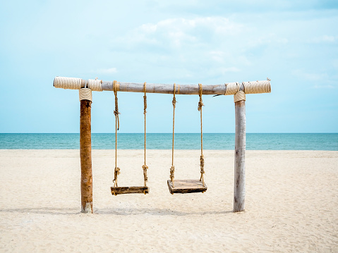 Empty wooden twin swing seat on the beach on seascape, sand, sea and blue sky background, minimal style.
