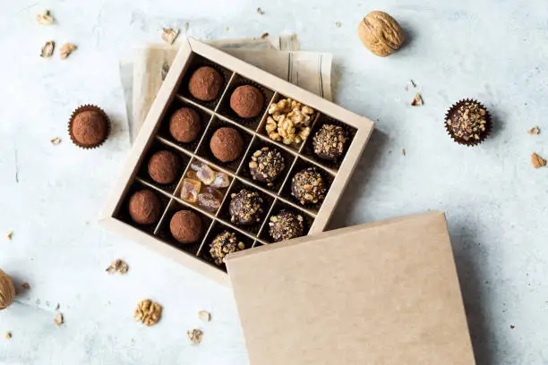 Chocolate truffle balls with cocoa powder in blank craft paper box, sweet delicious gift dessert for winter hoildays on marble background, shallow depth and selective focus